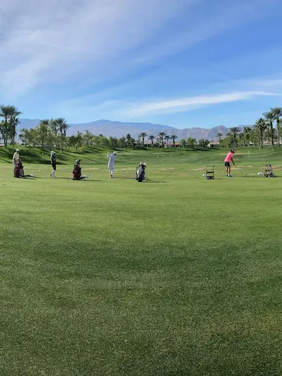 four golfers in a golf driving range, located outside with mountains in the background.